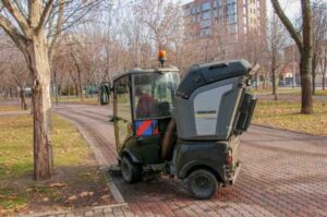 Small parking lot sweeping machine in park scrubbing tiled floor.