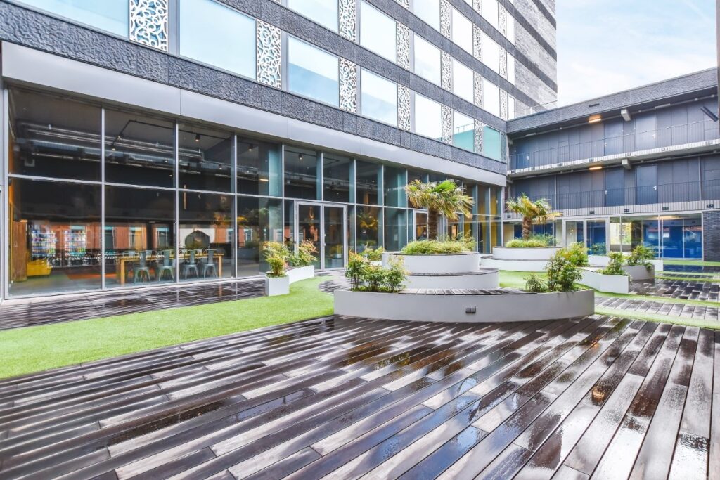 Green courtyard-of-the-building with wooden outdoors and green grass with small trees around courtyard