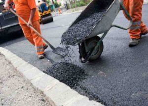 Two construction workers putting a wheel barrow of asphalt on the pavement
