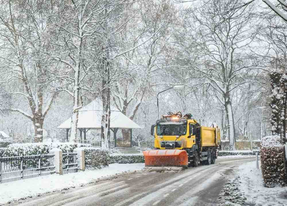 snow clearing services​ being done by yellow truck as it drives on road