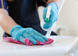 Person wearing blue rubber gloves disinfecting the surface with spray bottle and cleaning rag