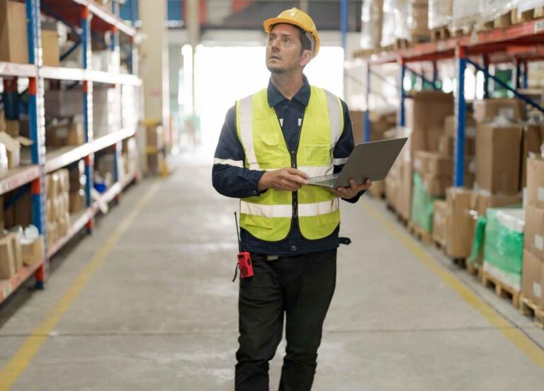 A man in safety wear walks in warehouse between isles