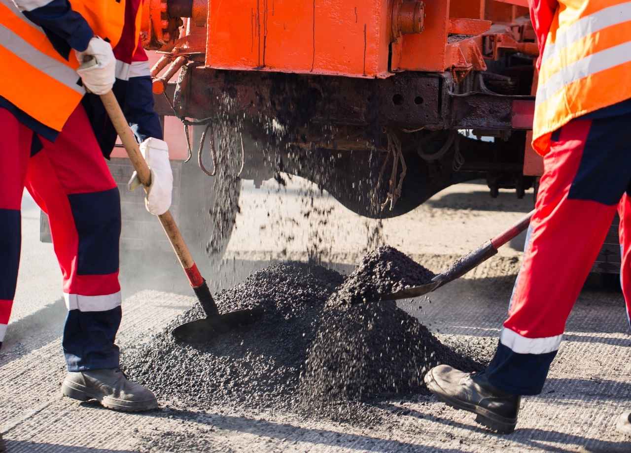 Two workers in safety gear shoveling asphalt
