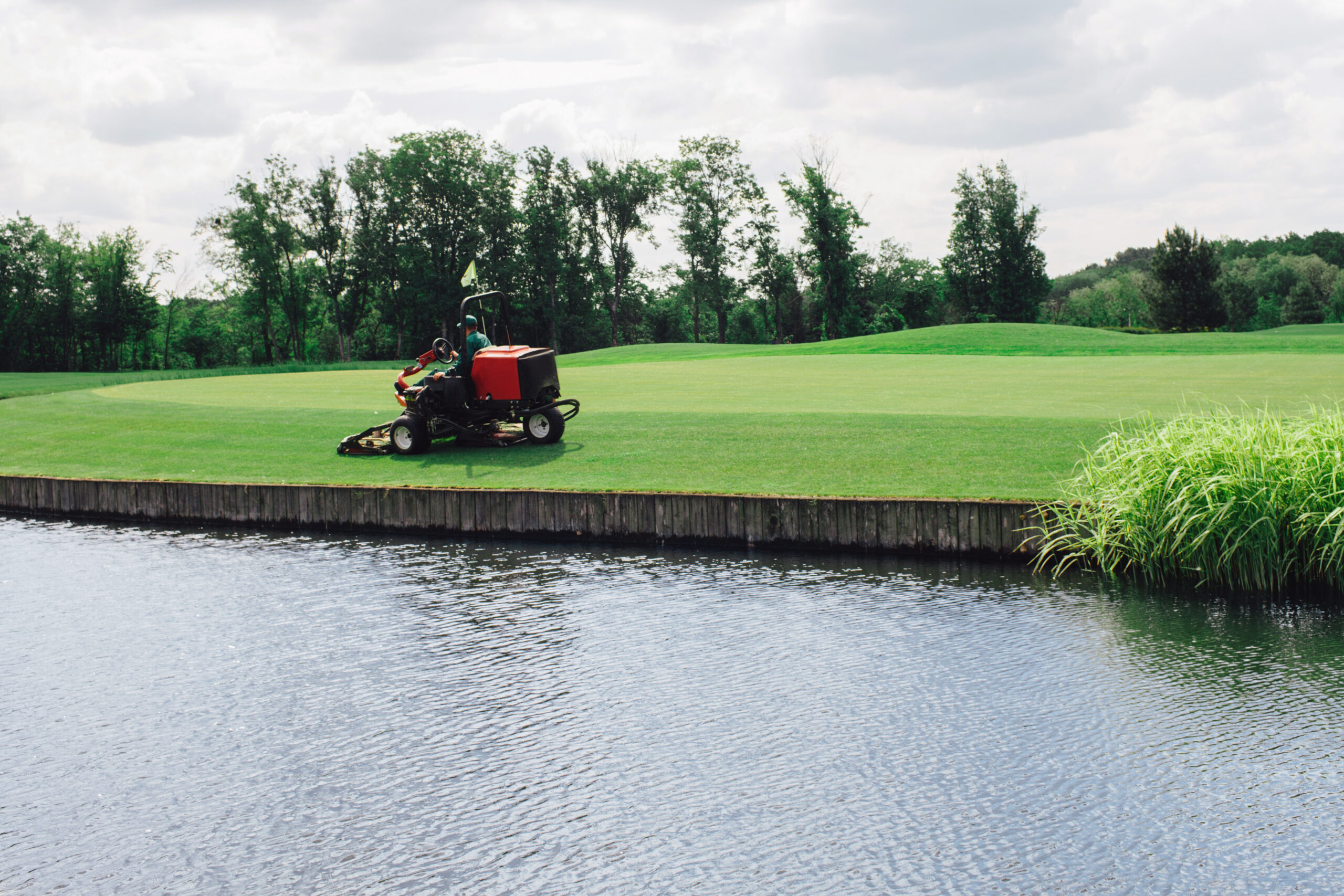 mowing lawn on golf course with pool of water beside it