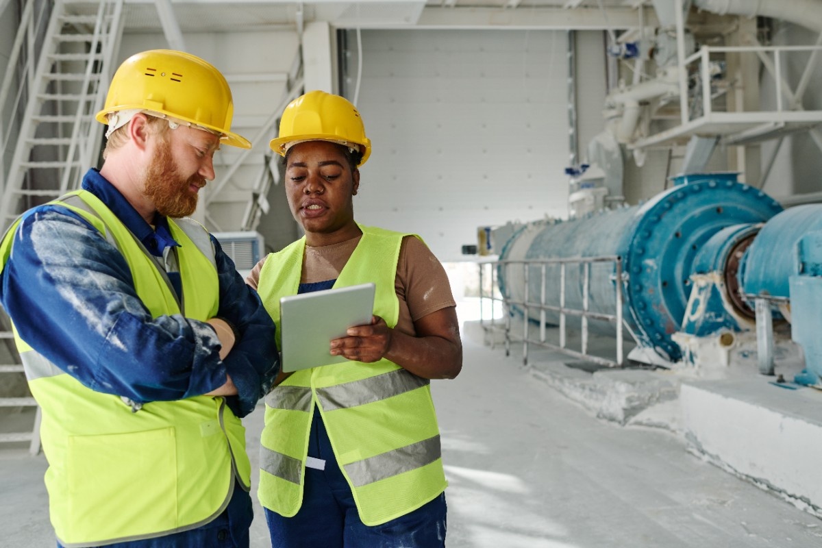 young woman showing a man something on her ipad both are dressed in safety wear