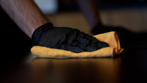 yellow rag cleaning and sanitizing a table held by a hand wearing a black rubber glove