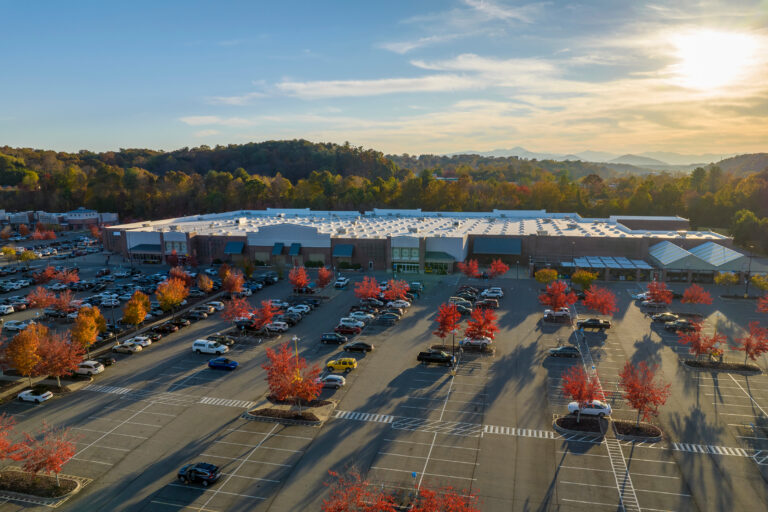 Aerial view of large parking lot in front of rgocery store with many parked colorful cars. Carpark at supercenter shopping mall with lines and markings for vehicle parking spaces and directions.