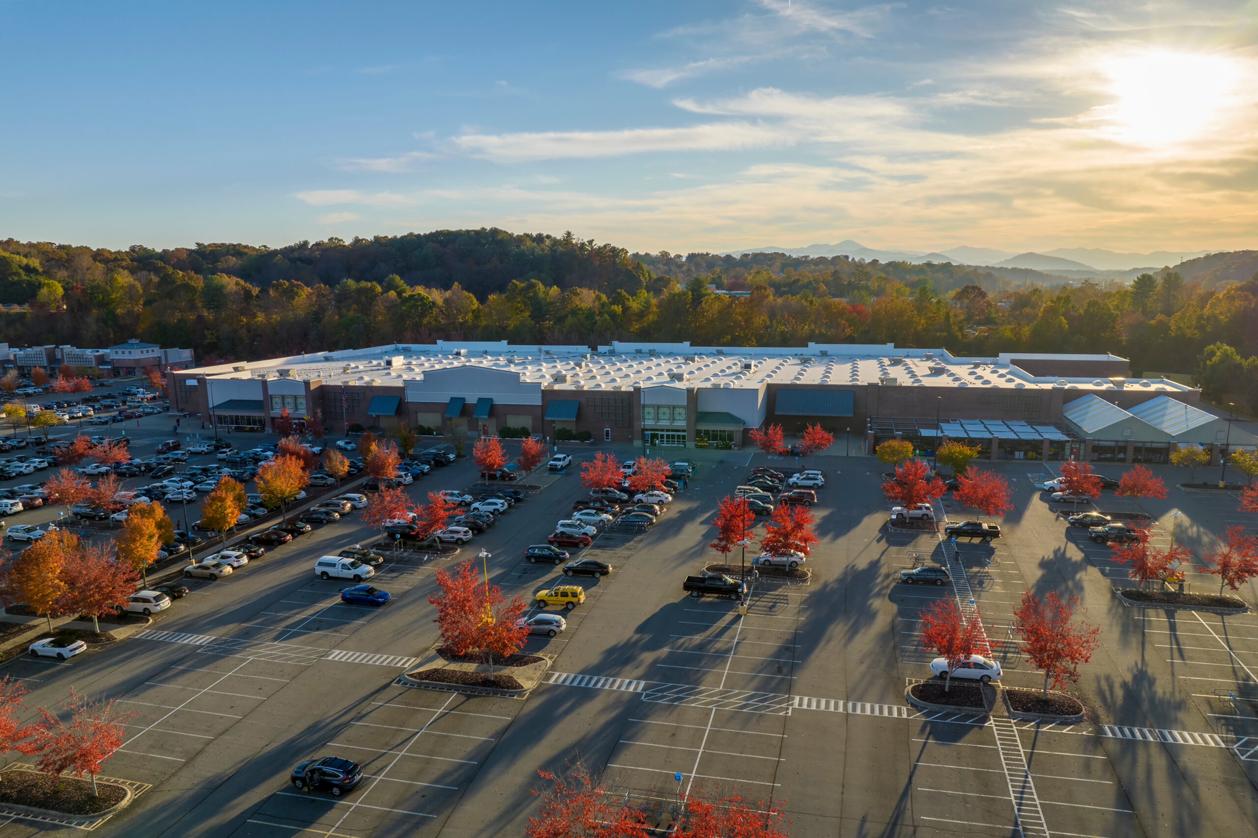 Aerial view of large parking lot in front of rgocery store with many parked colorful cars. Carpark at supercenter shopping mall with lines and markings for vehicle parking spaces and directions.