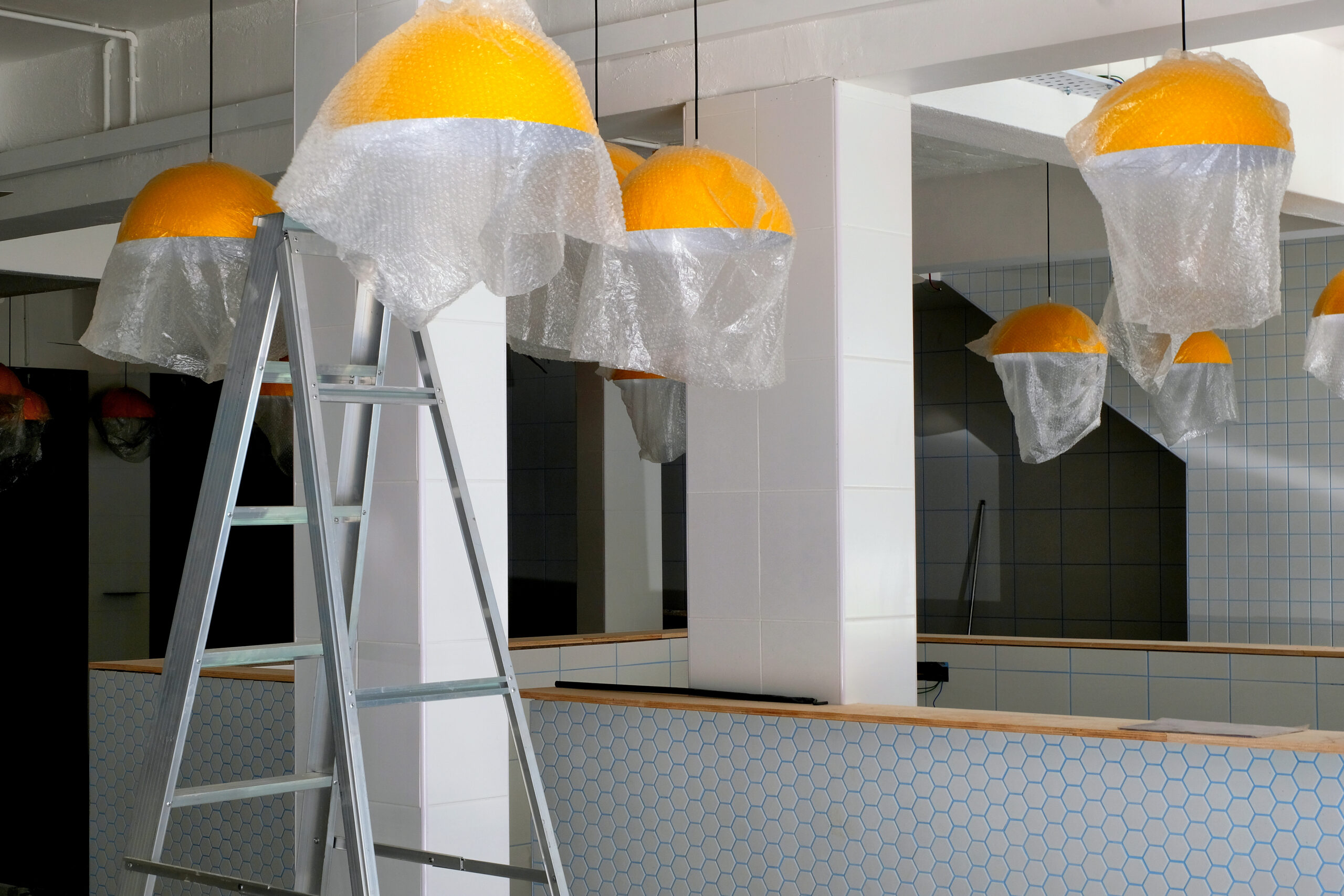An empty restaurant with covered yellow light fixtures is in mid renovation and remodel