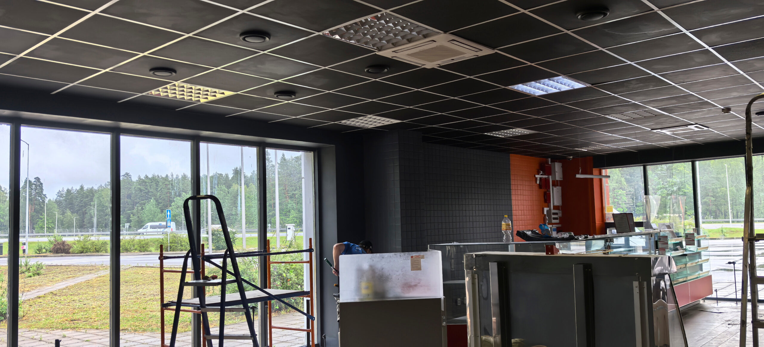 Inside a newly constructed space, workers set up large display cases while preparing for opening day. Natural light floods in through the expansive windows.