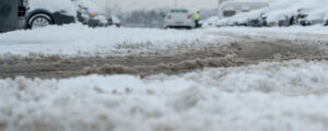 Muddy splush on wet urban road with car track on parking lot in winter or spring season