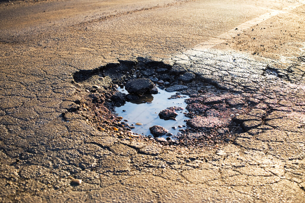 Water pooling in a pothole surrounded by cracked asphalt in a parking lot