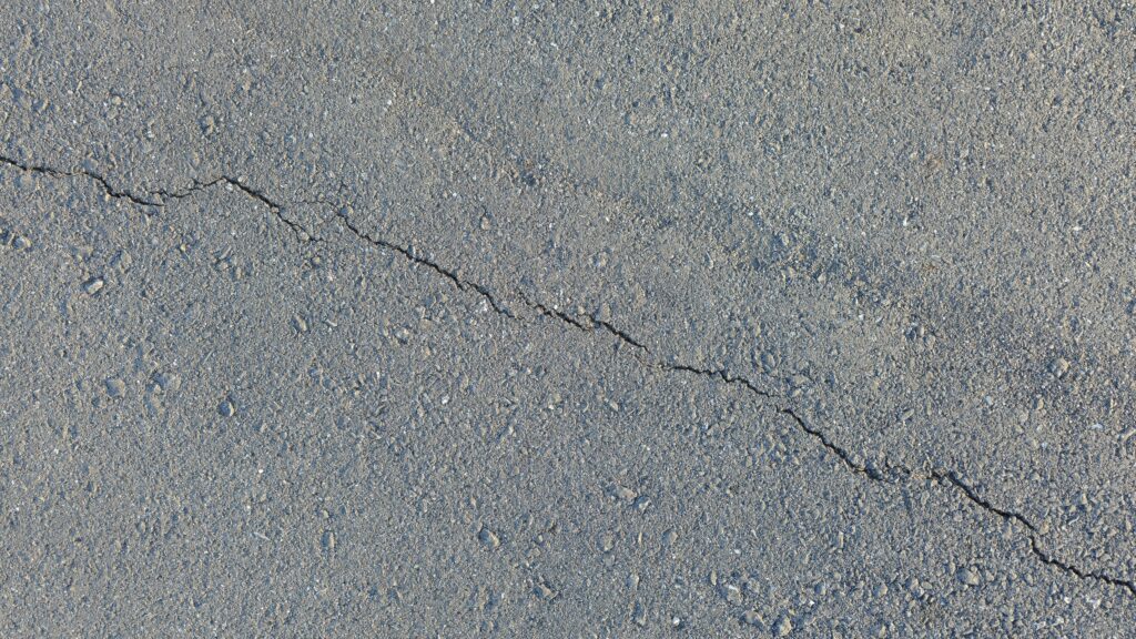 Close-up photo of a gray asphalt surface with fine aggregate. A small crack runs diagonally across the image. Ideal for use as a background or texture.