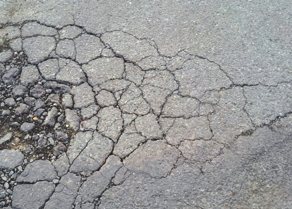 Damaged asphalt road surface with severe alligator cracking pattern.
