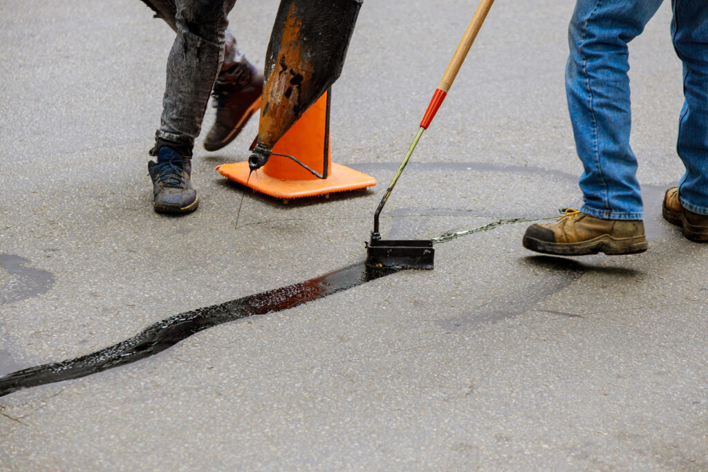 Road surface restoration work in the worker performs on road patcher work on the repair of cracks by filling and sealing with coated by bitumen emulsion asphalt surface.